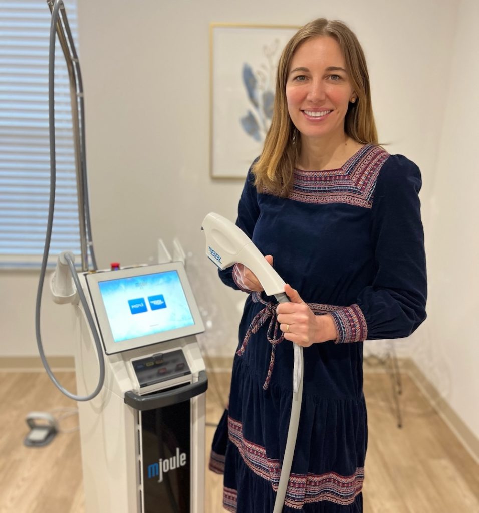 Mindy Jacques, MD stands with Sciton mJOULE laser, holding the BBL handpick in a treatment room.