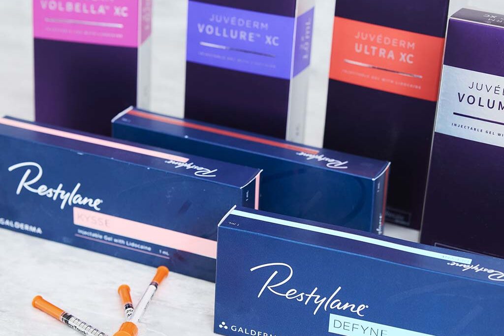 Boxes of Juvederm and Restylane facial fillers on counter in treatment room with syringes.